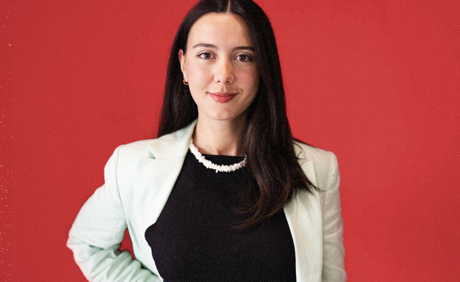 Foto de biografia da Leonor Caldeira. A Leonor aparece a meio corpo, a olhar directamente para a camera, com um sorriso confiante e um blazer branco, contra um fundo vermelho.